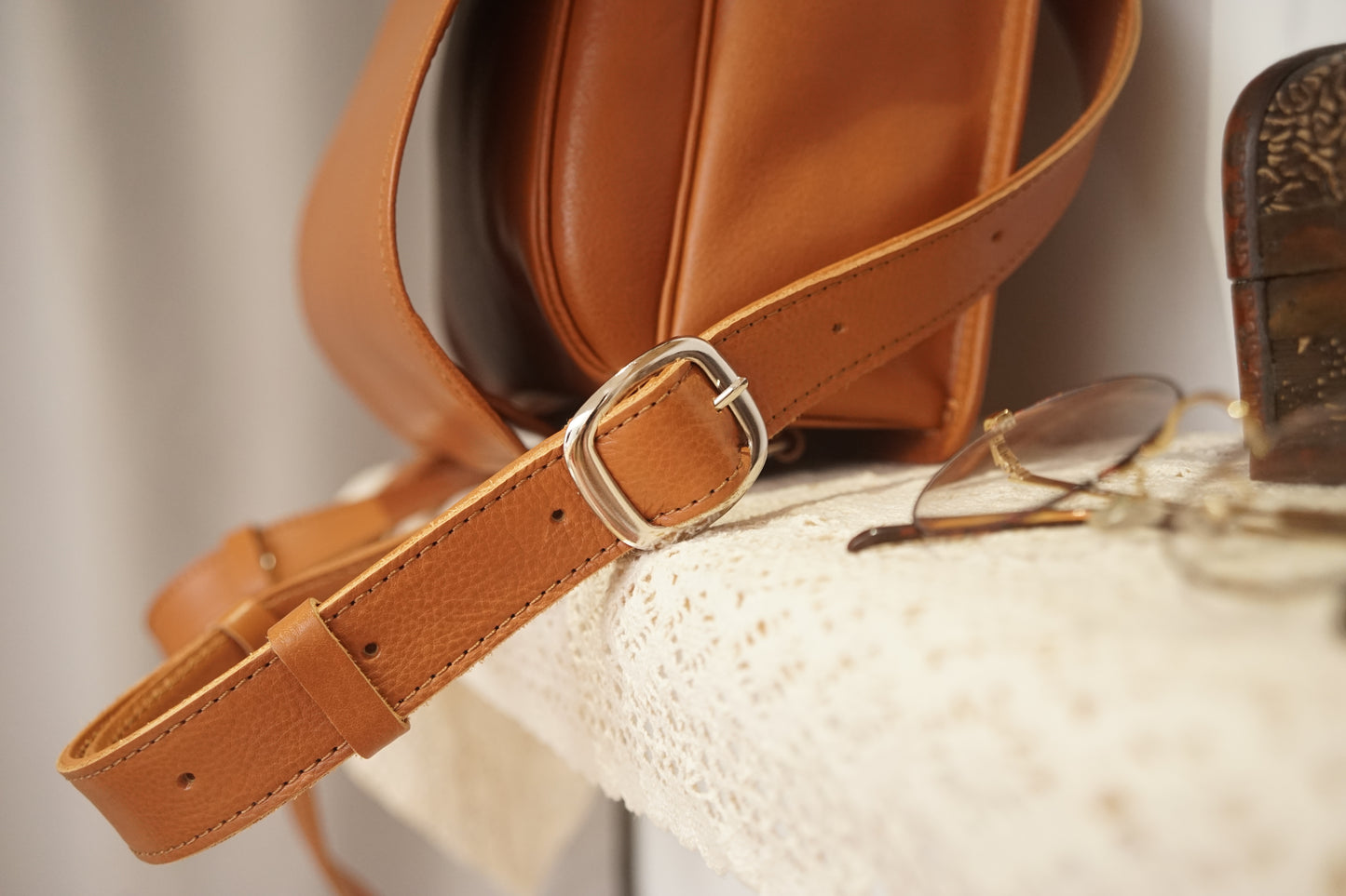 Brown leather bag with a strap and glasses on a textured surface