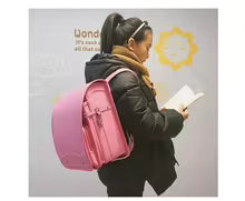 A Kid Is Wearing a Pink Backpack and Reading a Book